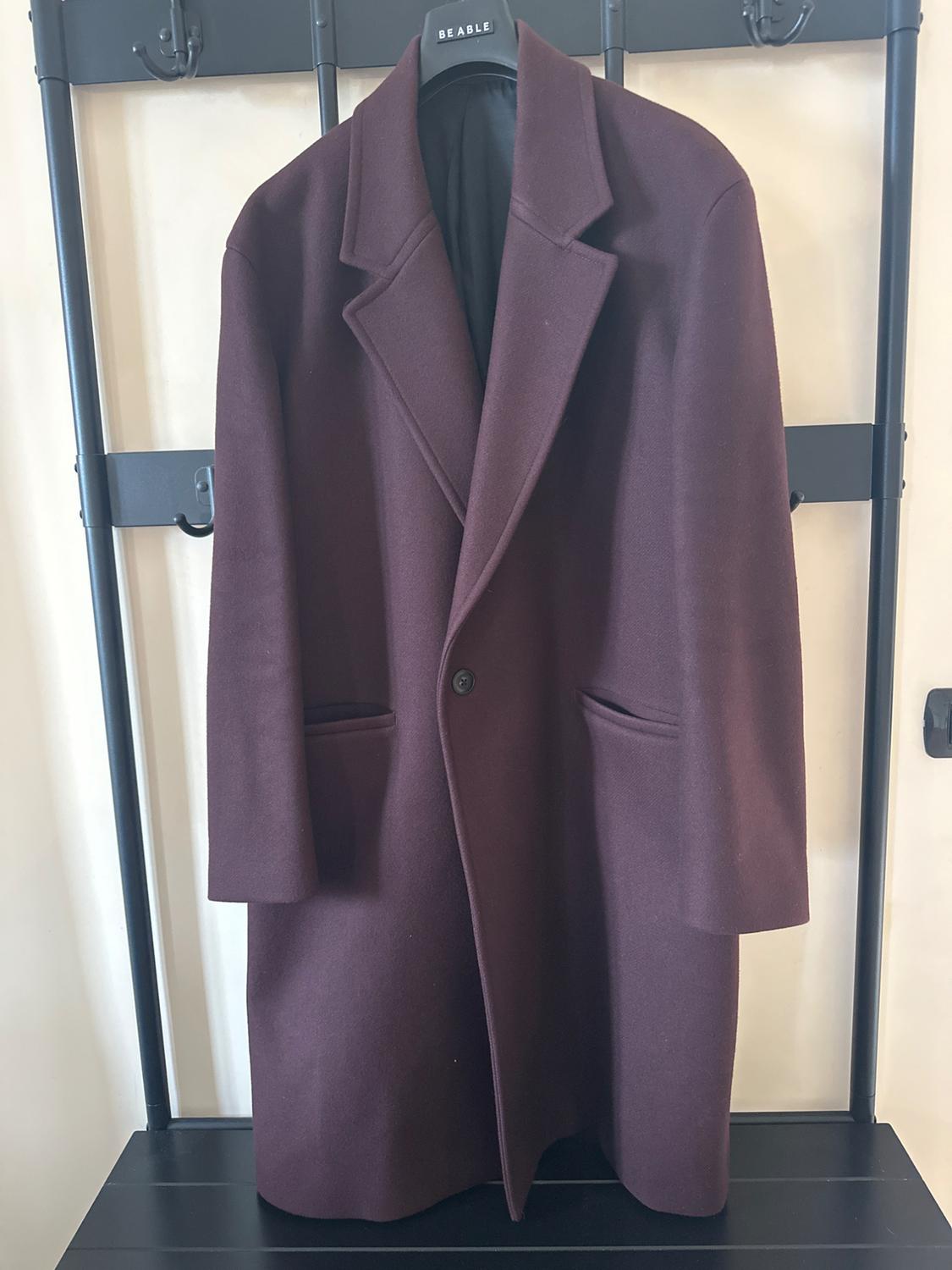 Long burgundy coat hanging on a black hanger with the "BEABLE" brand visible, against a light background and metal structure.