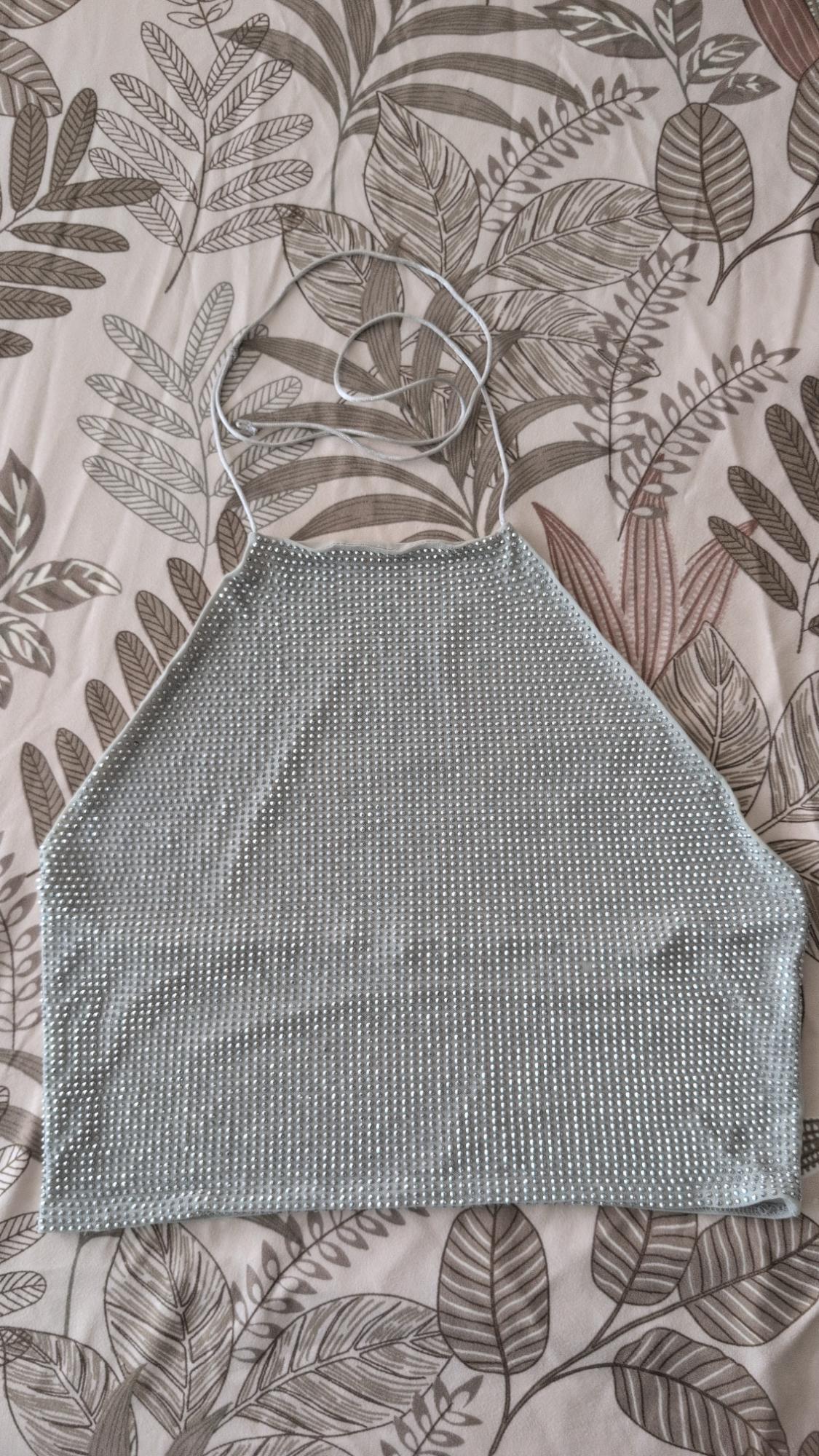 Shiny silver halter top against a leaf-print fabric background.