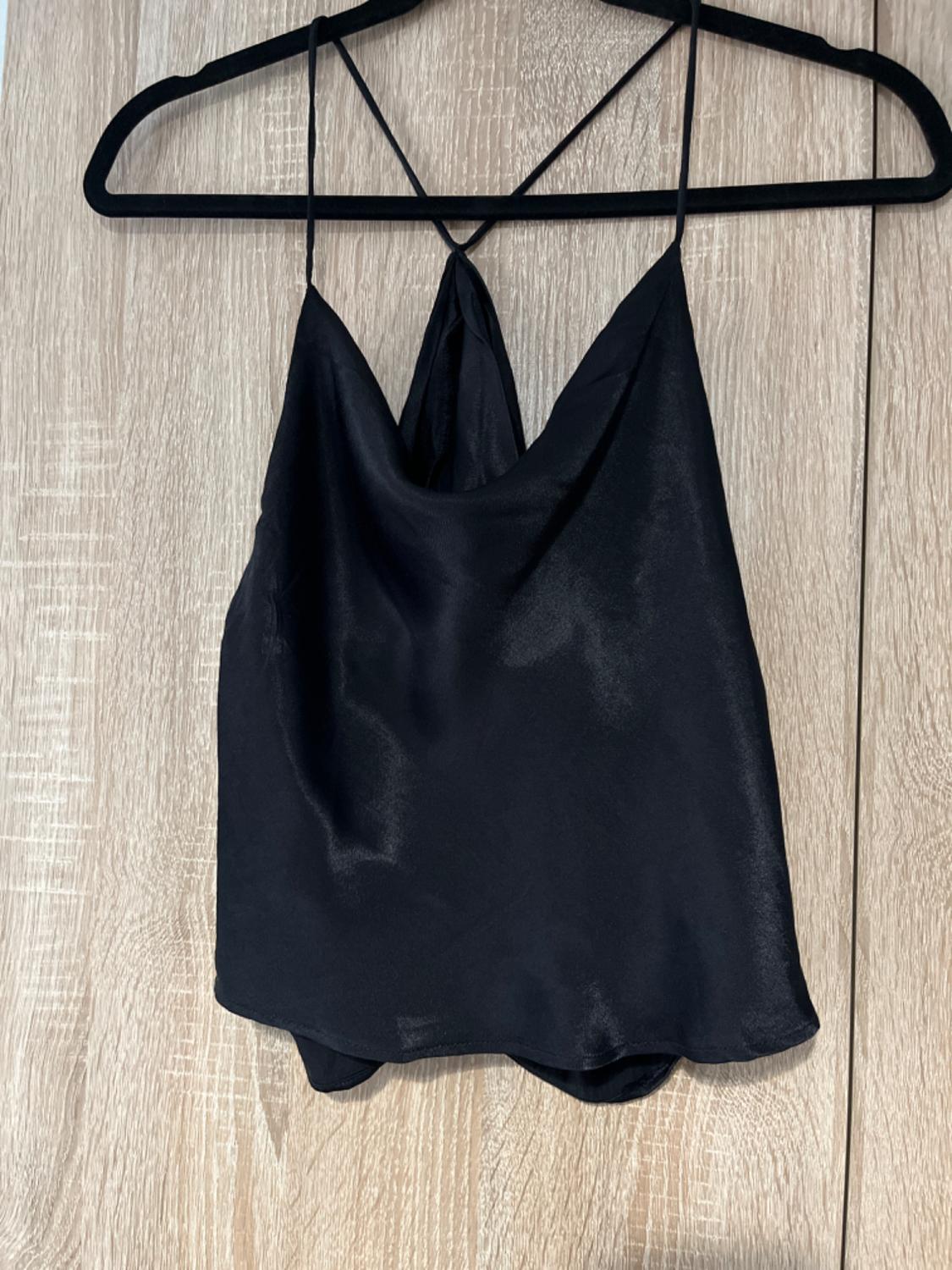 Front view of a black top with thin straps and a V-neck, hanging on a hanger.
