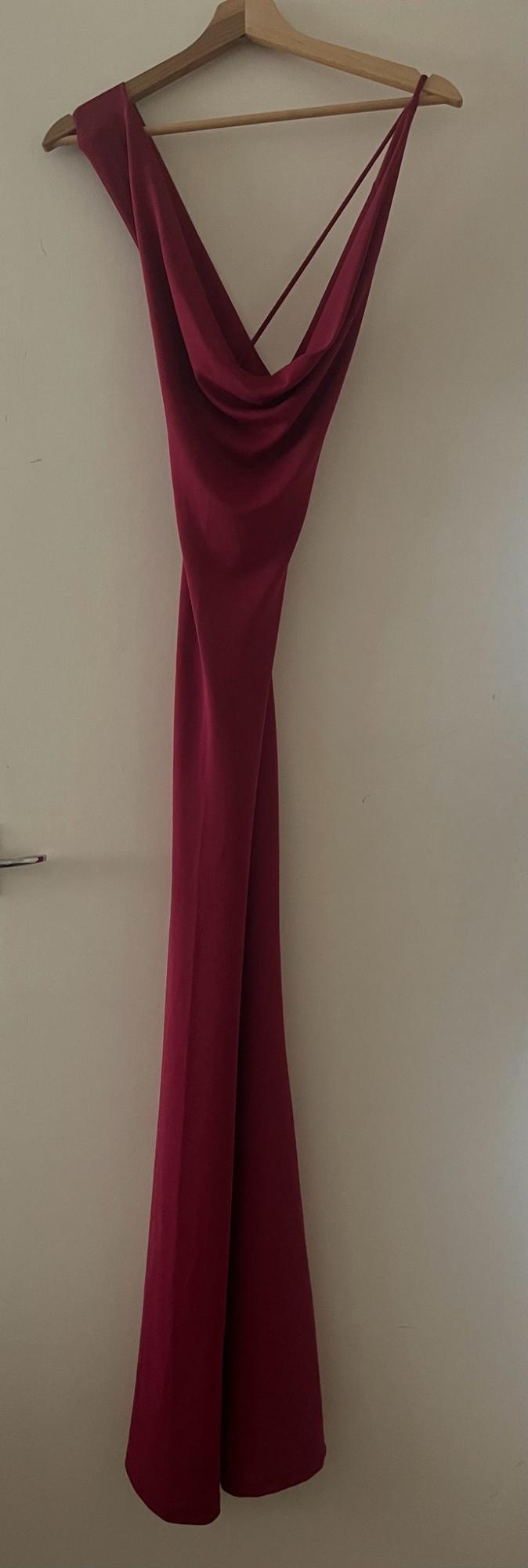 Burgundy long dress with a draped neckline hanging from a wooden hanger on a white door. Elegant and relaxed style.