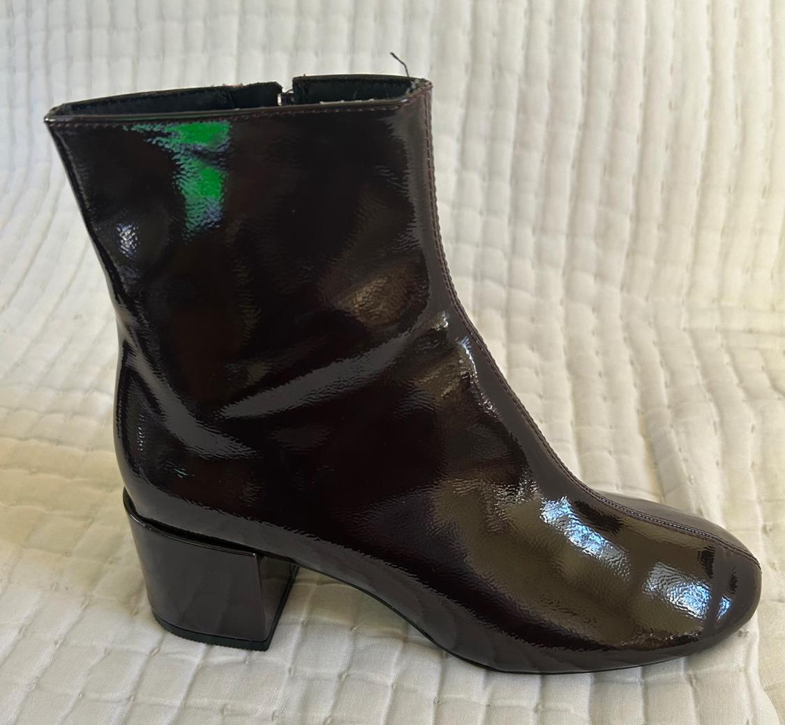 Side view of a dark patent leather boot with a square heel.