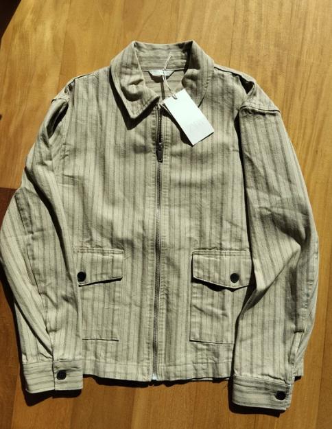 Vertical striped jacket in beige tones on a wooden surface. White tag hanging from the collar.