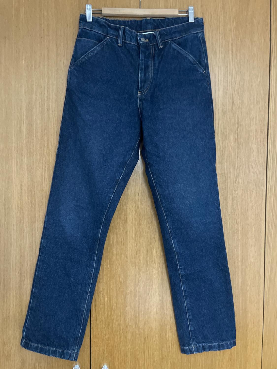 Blue jeans hanging on a wooden hanger against a light wooden background.