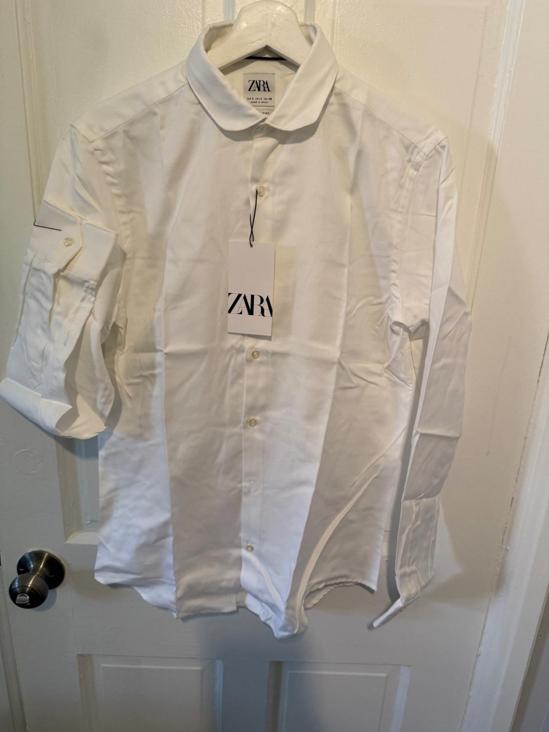 White long-sleeved shirt hanging on a white hanger over a door. Visible label with the text "ZARA".