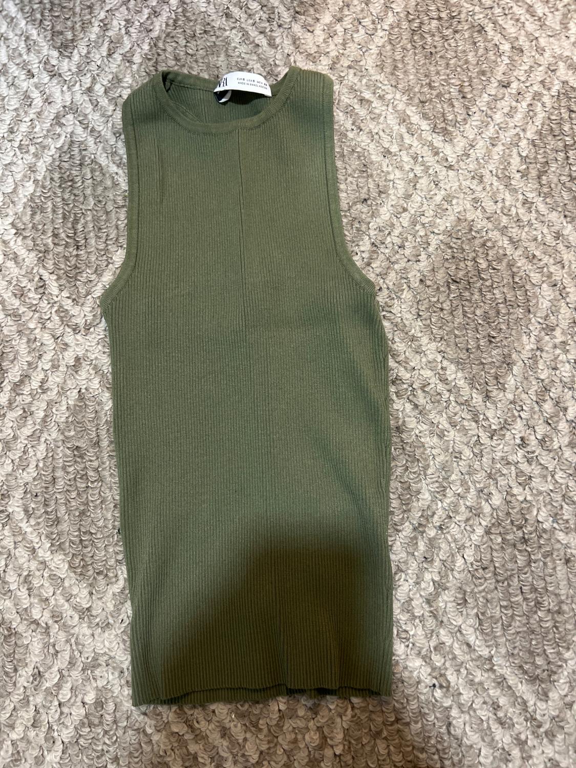 Olive green sleeveless top on textured grey carpet. Visible label at the neck.
