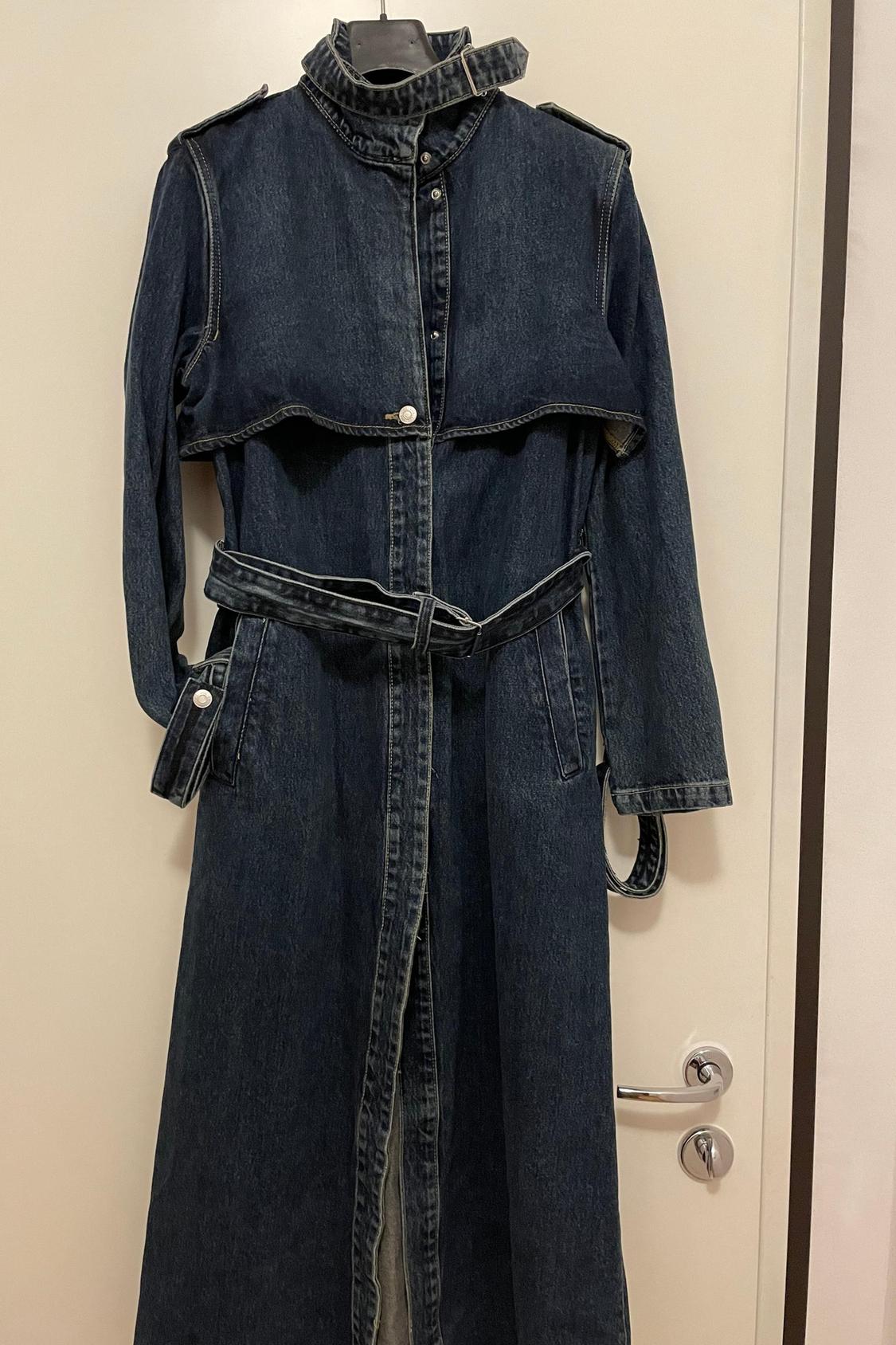Front view of dark blue denim long coat with a belt and side pockets.