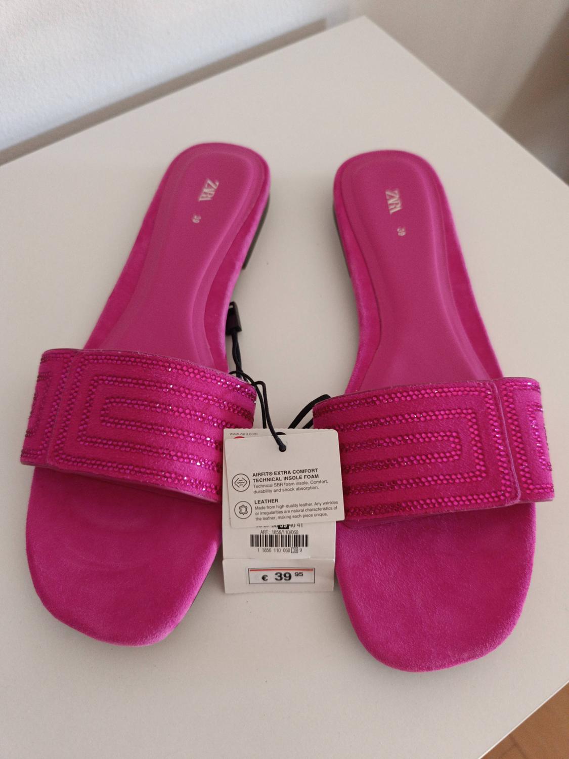 Pair of fuchsia flat sandals with a geometric glitter strap on a white surface. Visible text: ZARA 39, €39.95.
