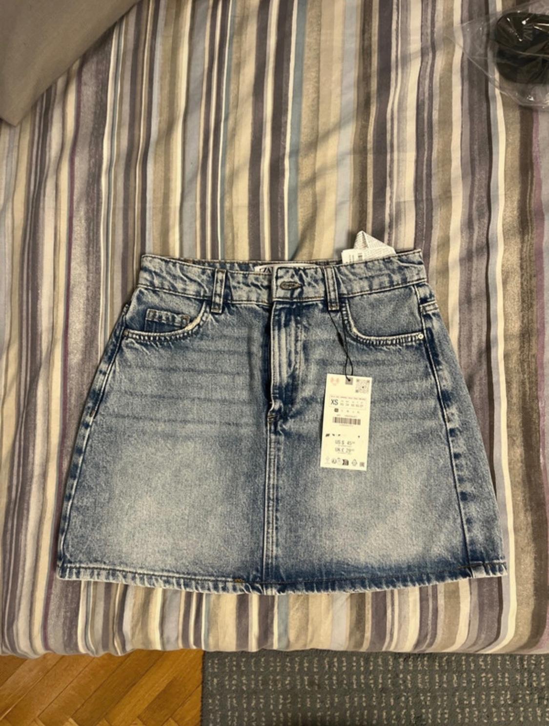 Light blue denim skirt with an XS size tag on a striped quilt in shades of grey and beige.