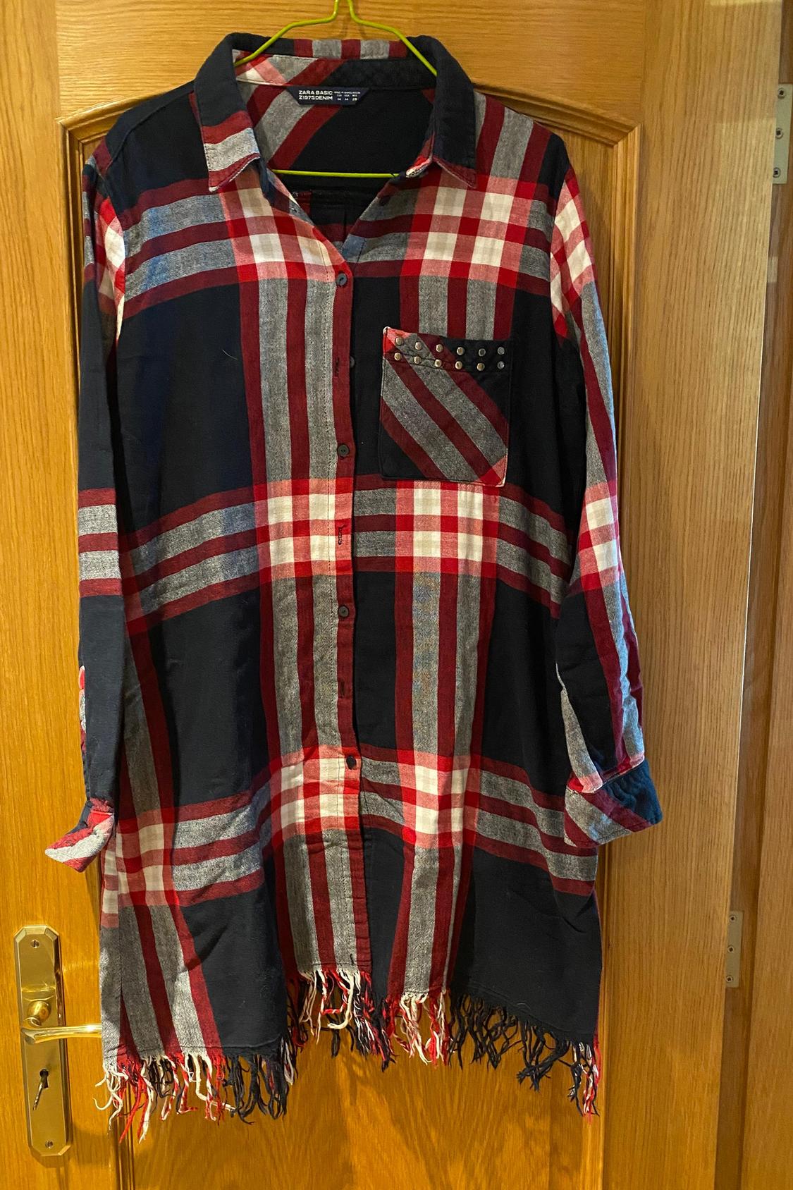 Front view of red and black checked long shirt with embellished front pocket and fringe on the hem.