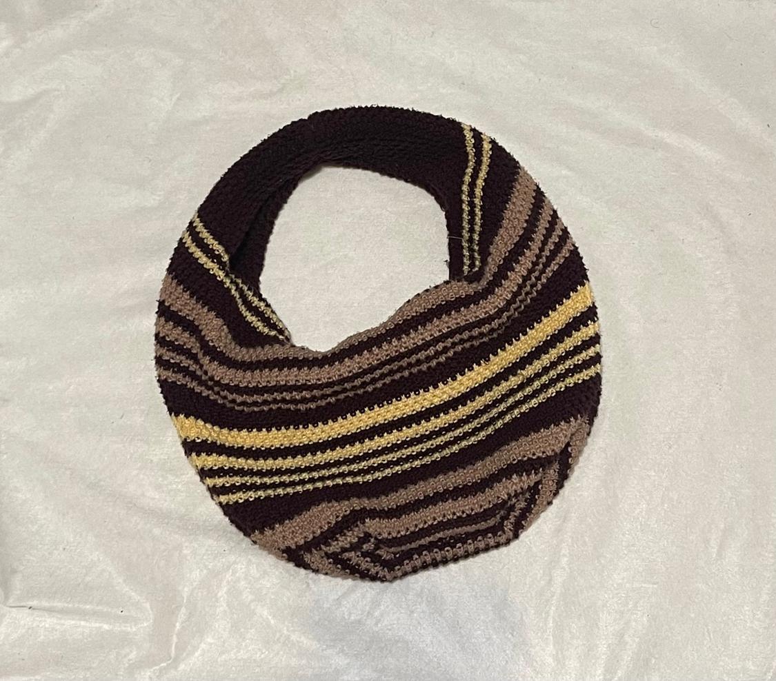 Striped knit bag in shades of brown and yellow on a white crinkled fabric background. Simple composition with a relaxed style.