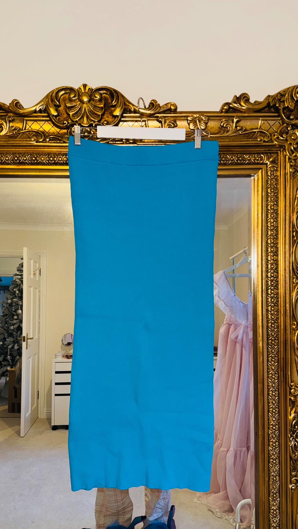 Blue skirt hanging on an ornate gold mirror. Reflection of a pink dress in the mirror. Room background with open door.
