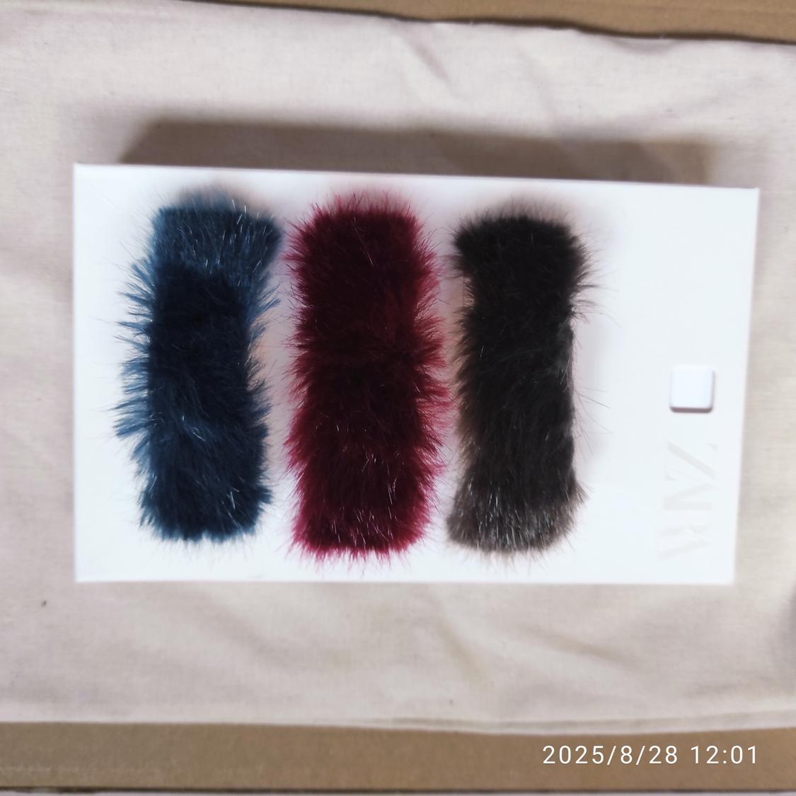 Three faux fur pom-poms in blue, red and black on a white background. Visible text: "ZARA". Date in the corner: "2025/8/28 12:01".