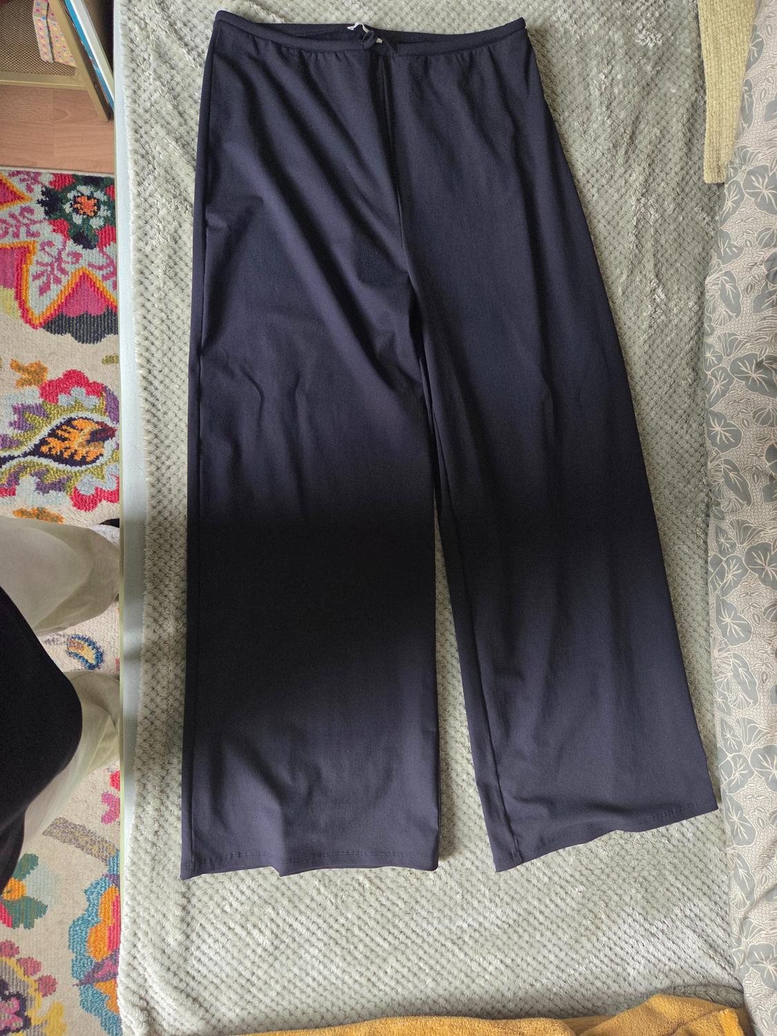 Dark wide-leg trousers laid out on a light textured blanket in a relaxed setting, next to a colourful rug.