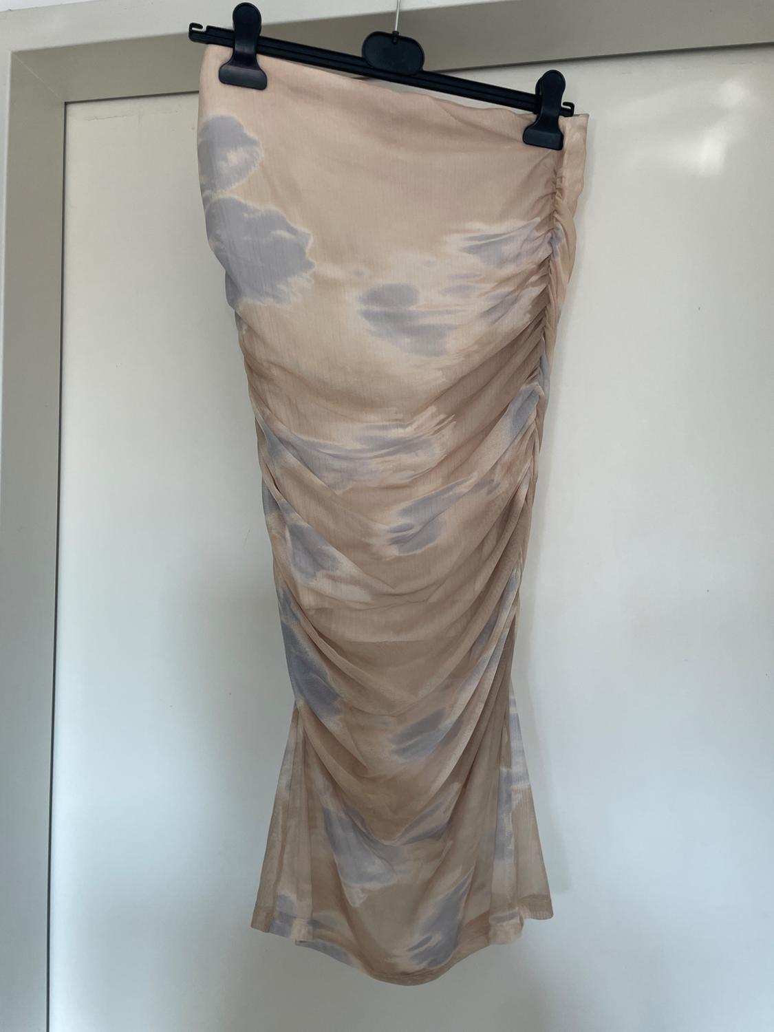 Beige skirt with grey cloud print, hanging on a black hanger against a white background. Draped and lightweight fabric.