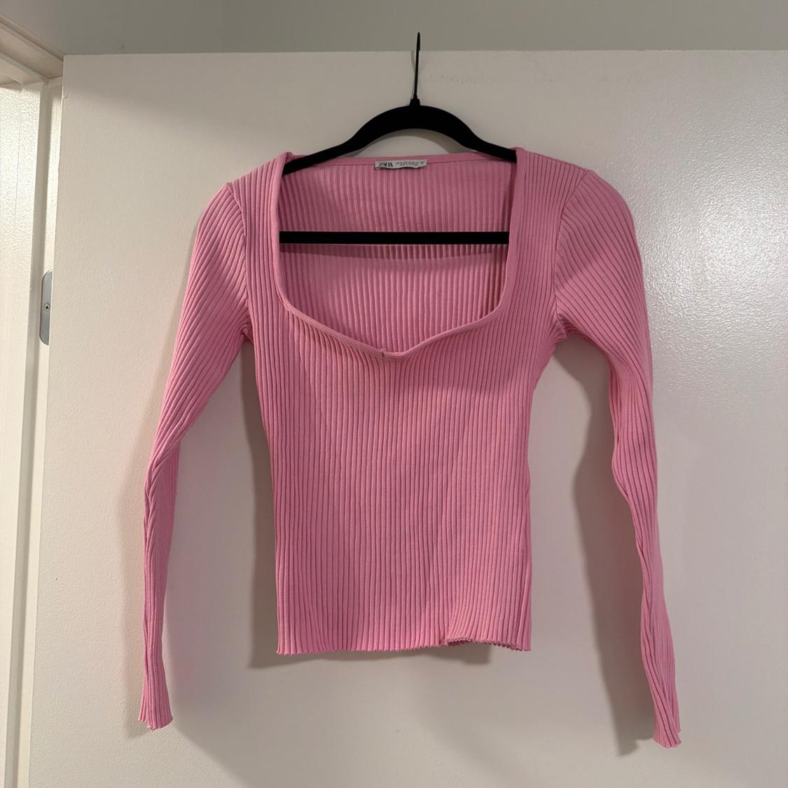 Pink ribbed knit top, long-sleeved with a wide neckline, hanging on a black hanger against a white door.
