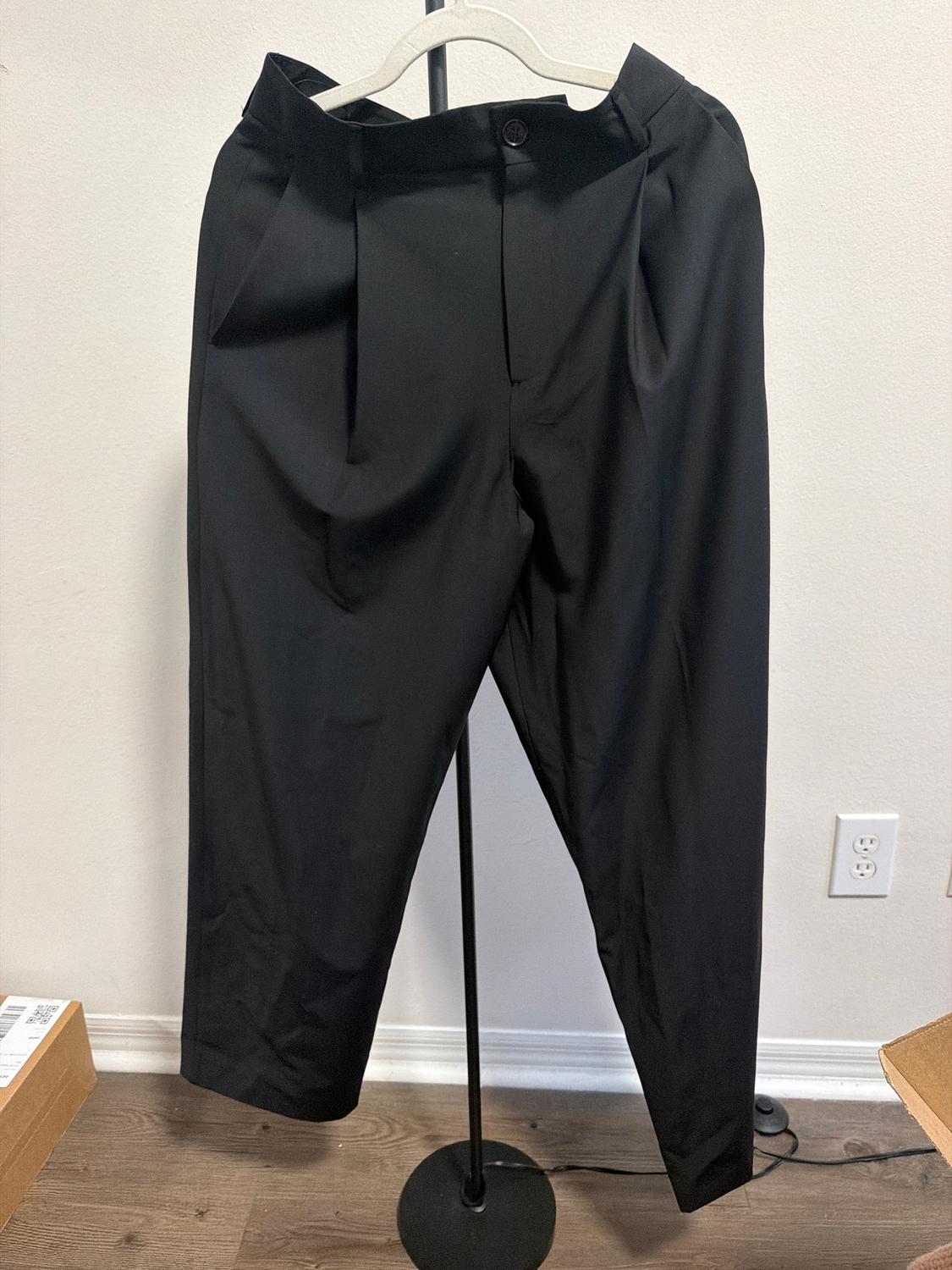 Black pants hanging on a hanger over a metal stand, white wall background and wooden floor.