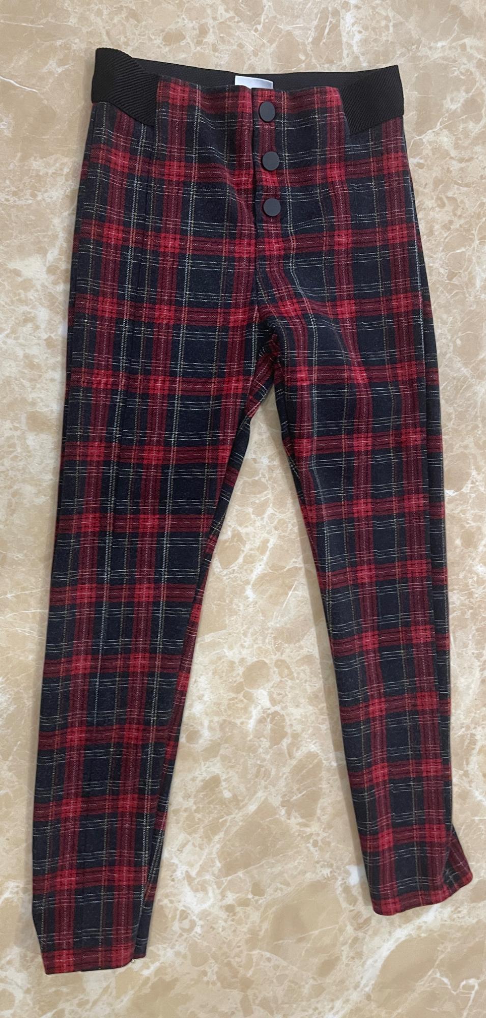 Red and black checked trousers with three front buttons and black elastic panels at the waist, on a light marble background.