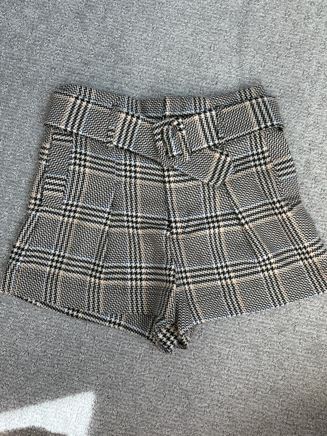 Plaid shorts in black and beige tones with a matching belt, on a gray rug.