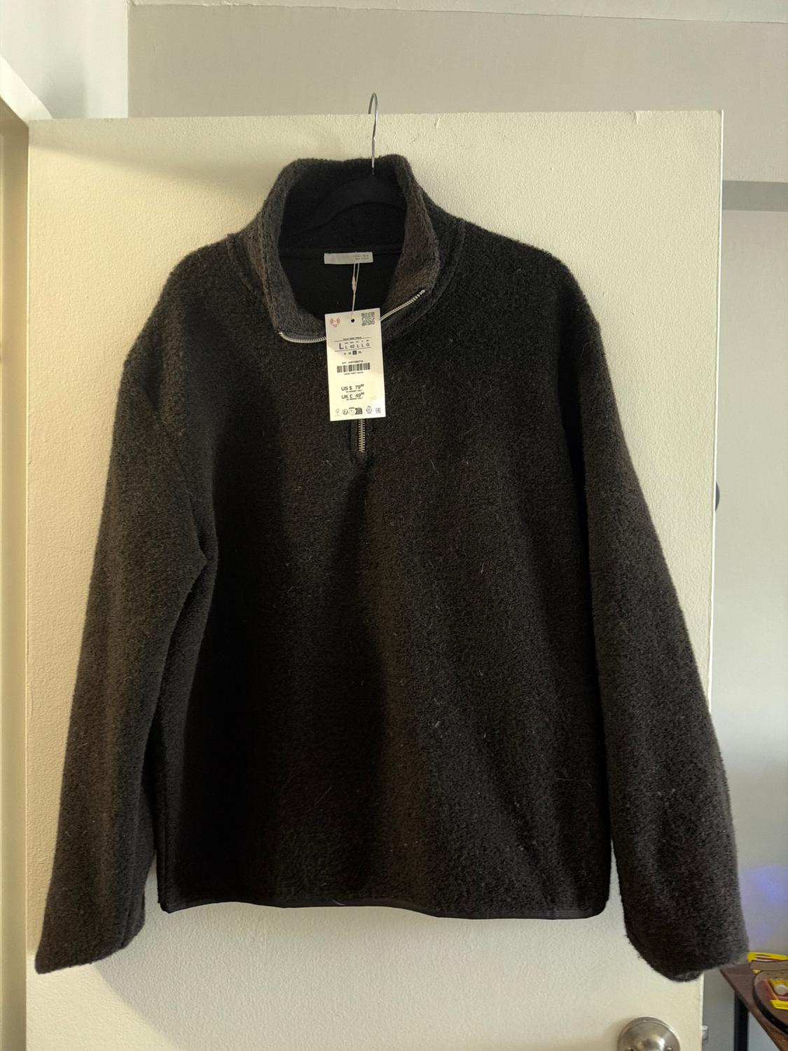 Black wool jumper hanging on a white door, with a visible label showing a barcode and large size.