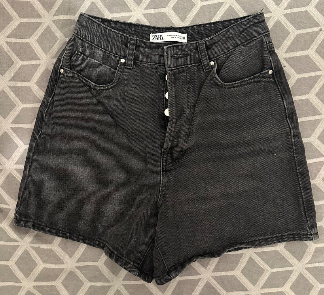 Black denim shorts with visible buttons, on a grey geometric background. Visible label: "ZARA".
