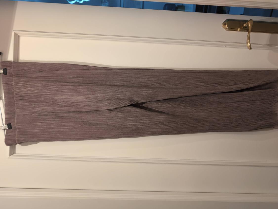 Pleated long trousers in a greyish-brown shade, held with pegs and hung over a white door with a gold handle.