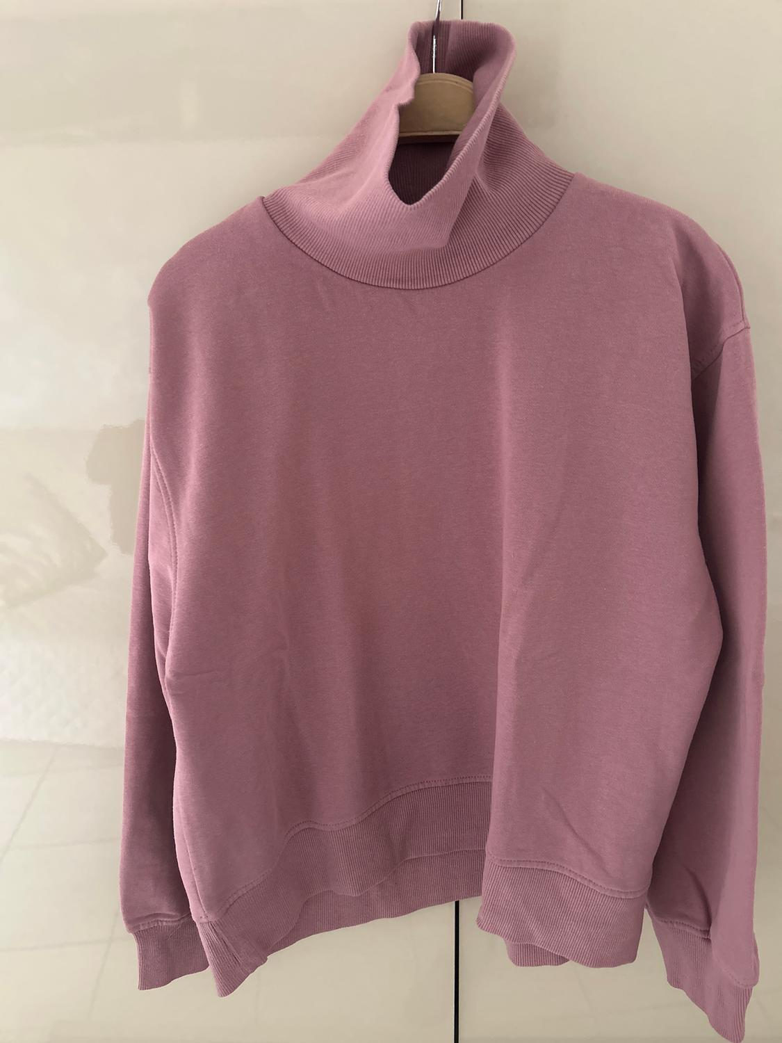 Pink polo neck jumper hanging on a wooden hanger against a light background.