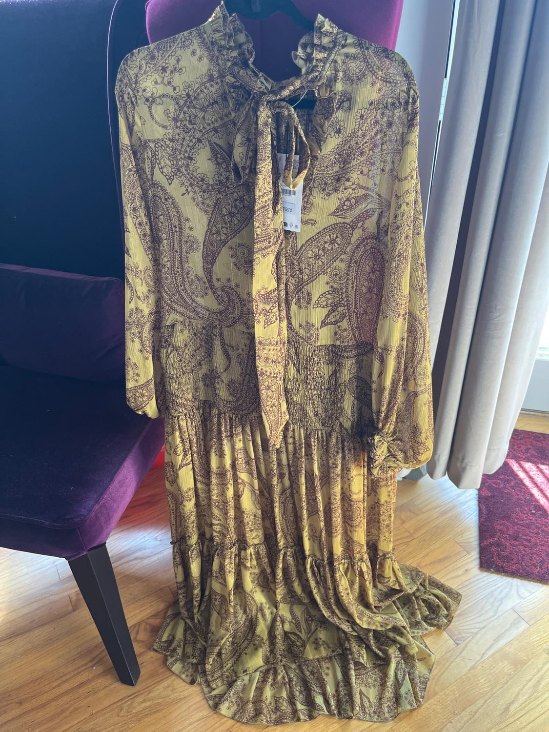 Long patterned dress in brown and yellow tones, hanging on a purple velvet chair, on a wooden floor.