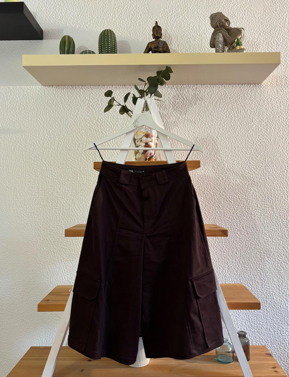 Brown shorts hanging on a white clothes rail, with wooden shelves behind, decorated with cacti and figurines.