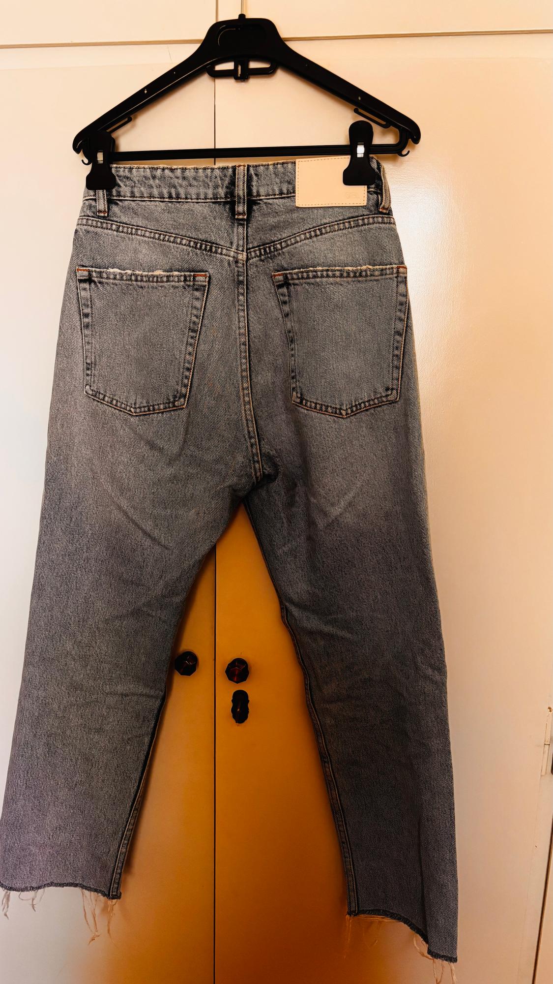 Light blue denim jeans hanging on a black hanger over a yellow door. The hems are frayed.