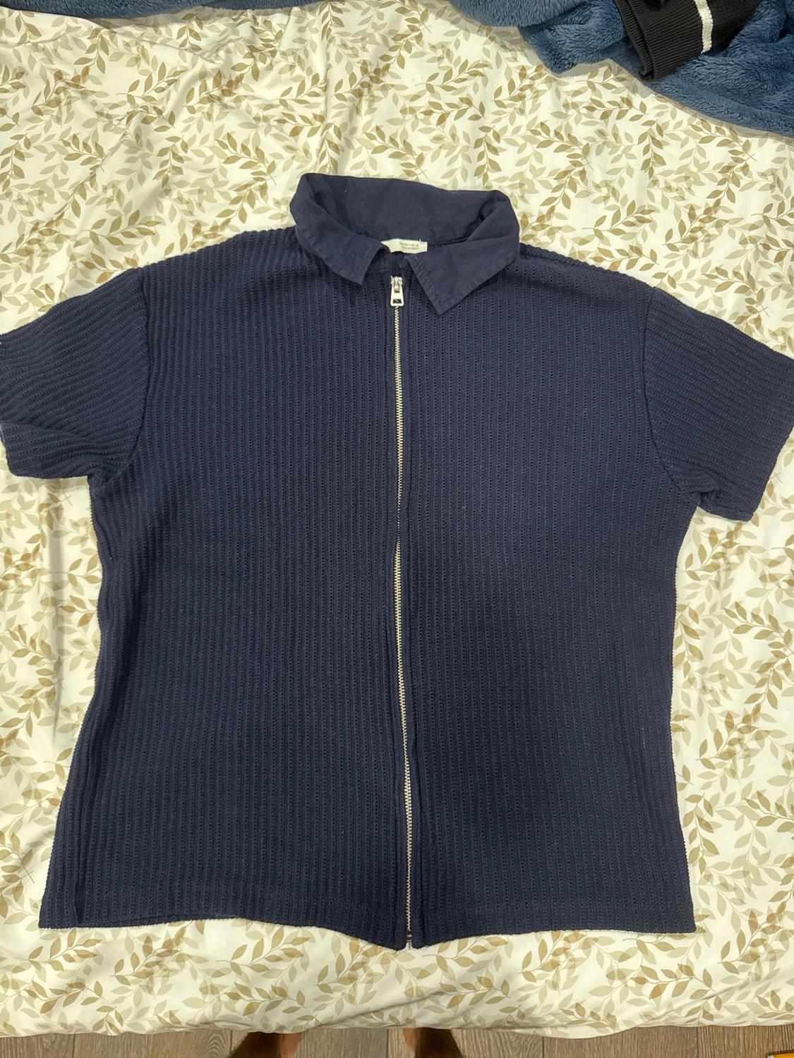 Navy blue short-sleeved shirt with a collar and front zip. Ribbed fabric. Resting on a leaf-print sheet.