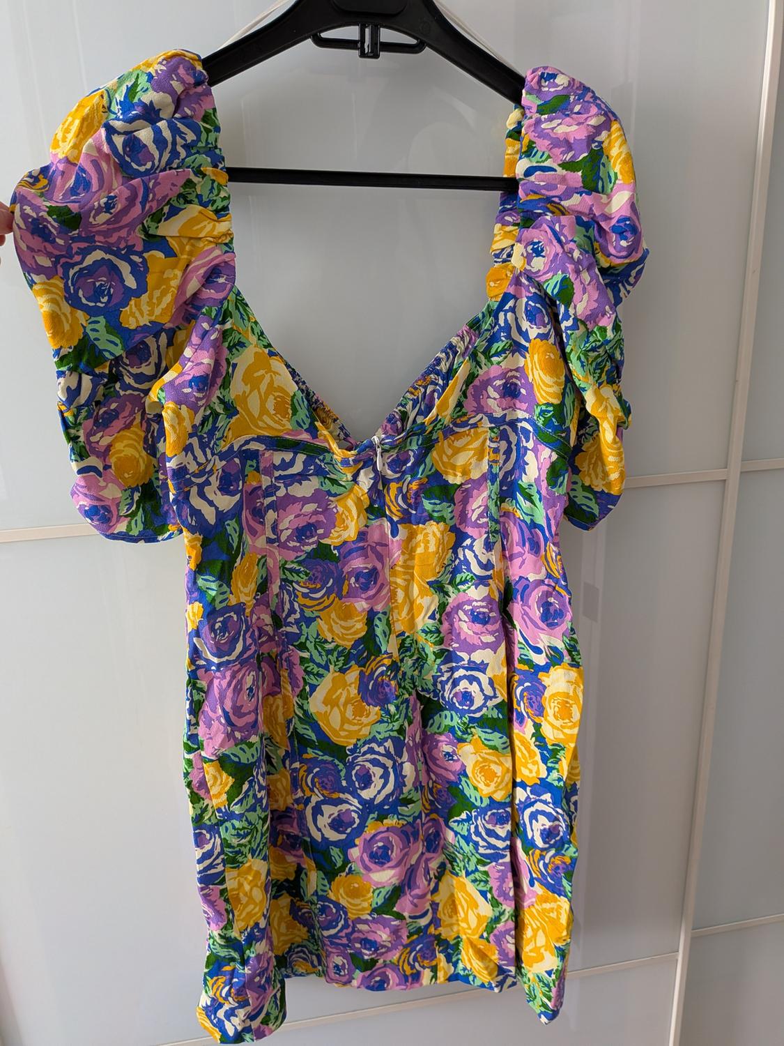 Floral print dress in shades of purple, yellow, and blue, hanging on a black hanger against a white background.