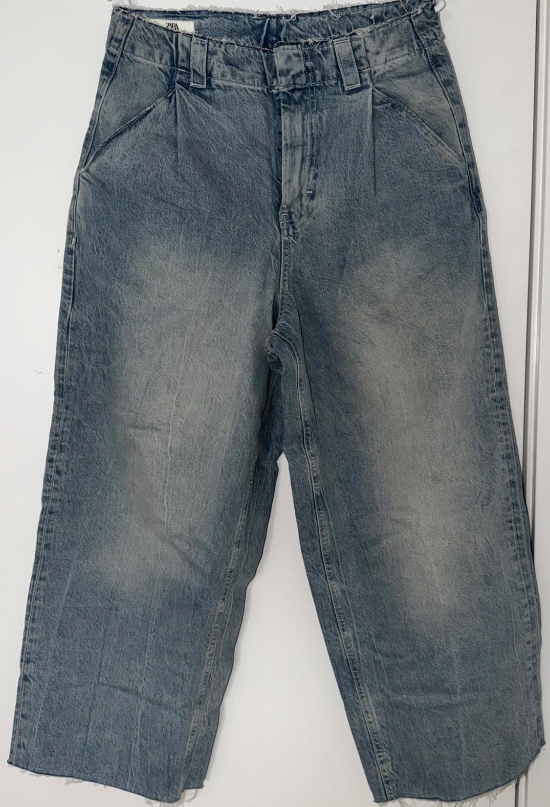 Wide, washed blue denim jeans with an elasticated waist and frayed hem, hanging on a white background.
