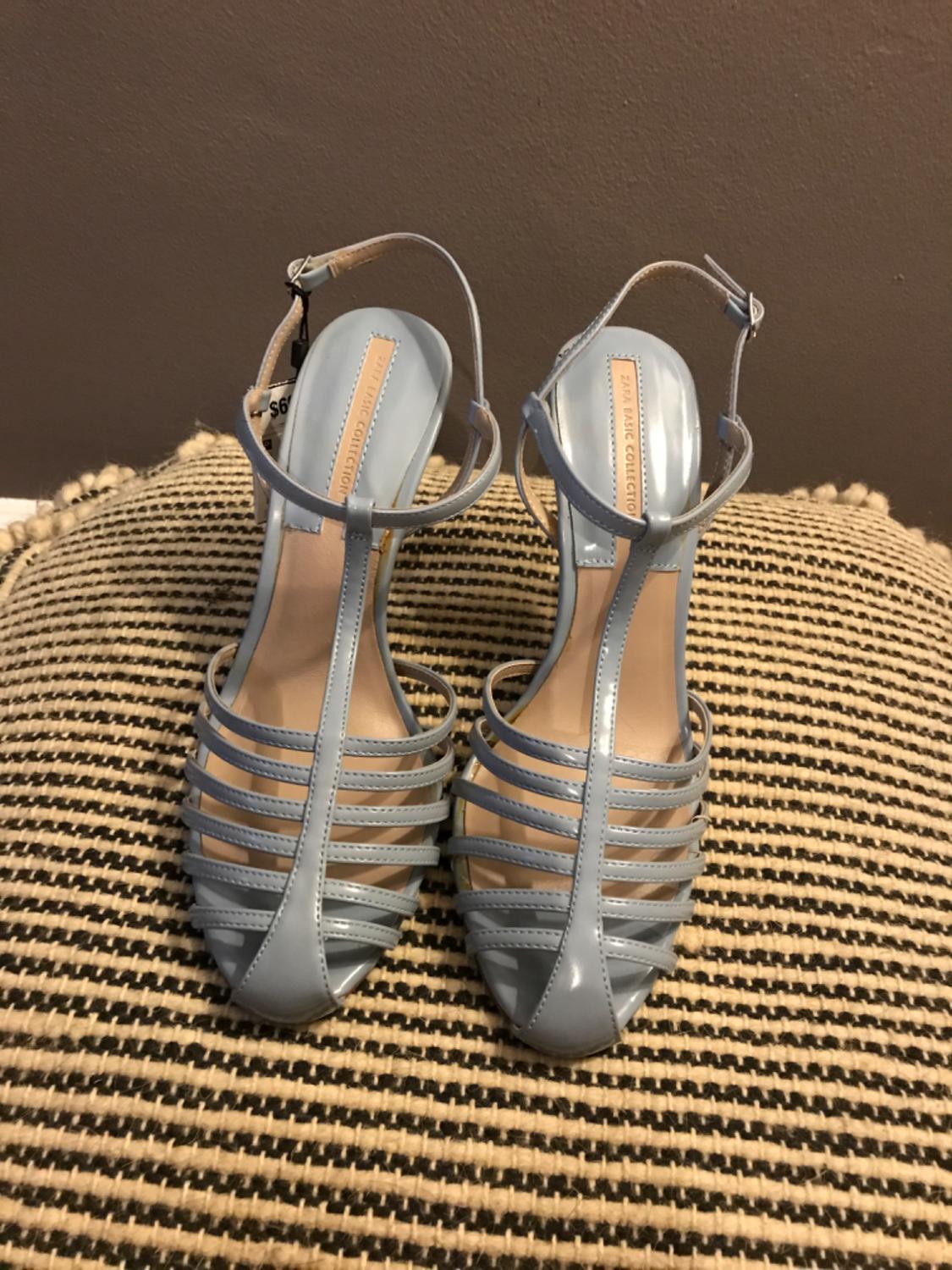 Front view of light blue sandals with crossed straps and buckles.