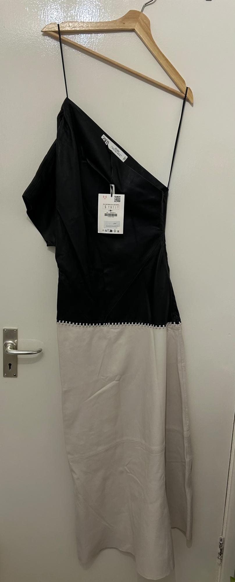 Dress hanging on a wooden hanger, with a black top and white skirt. Visible label with barcode and size S.