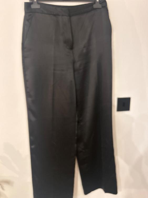 Black trousers hanging on a hanger against a white background. Smooth fabric and a straight cut, with visible side pockets.
