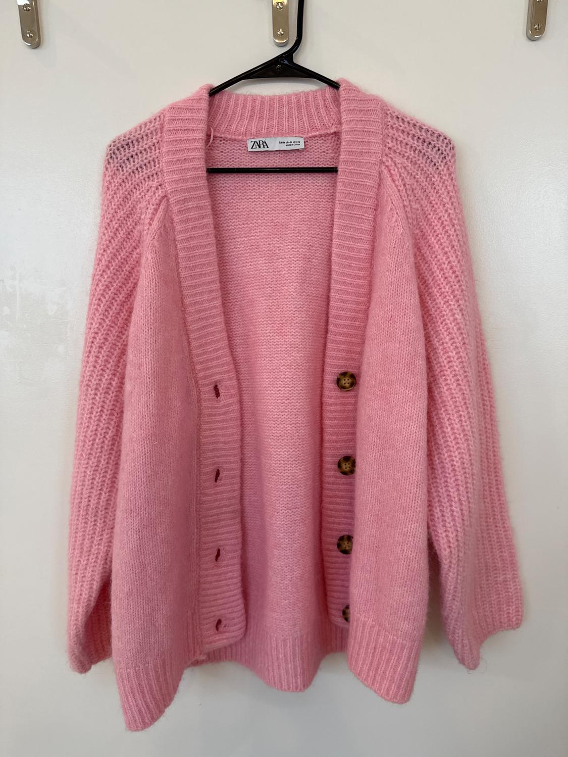 Front view of a pink cardigan with large brown buttons and chunky knit.