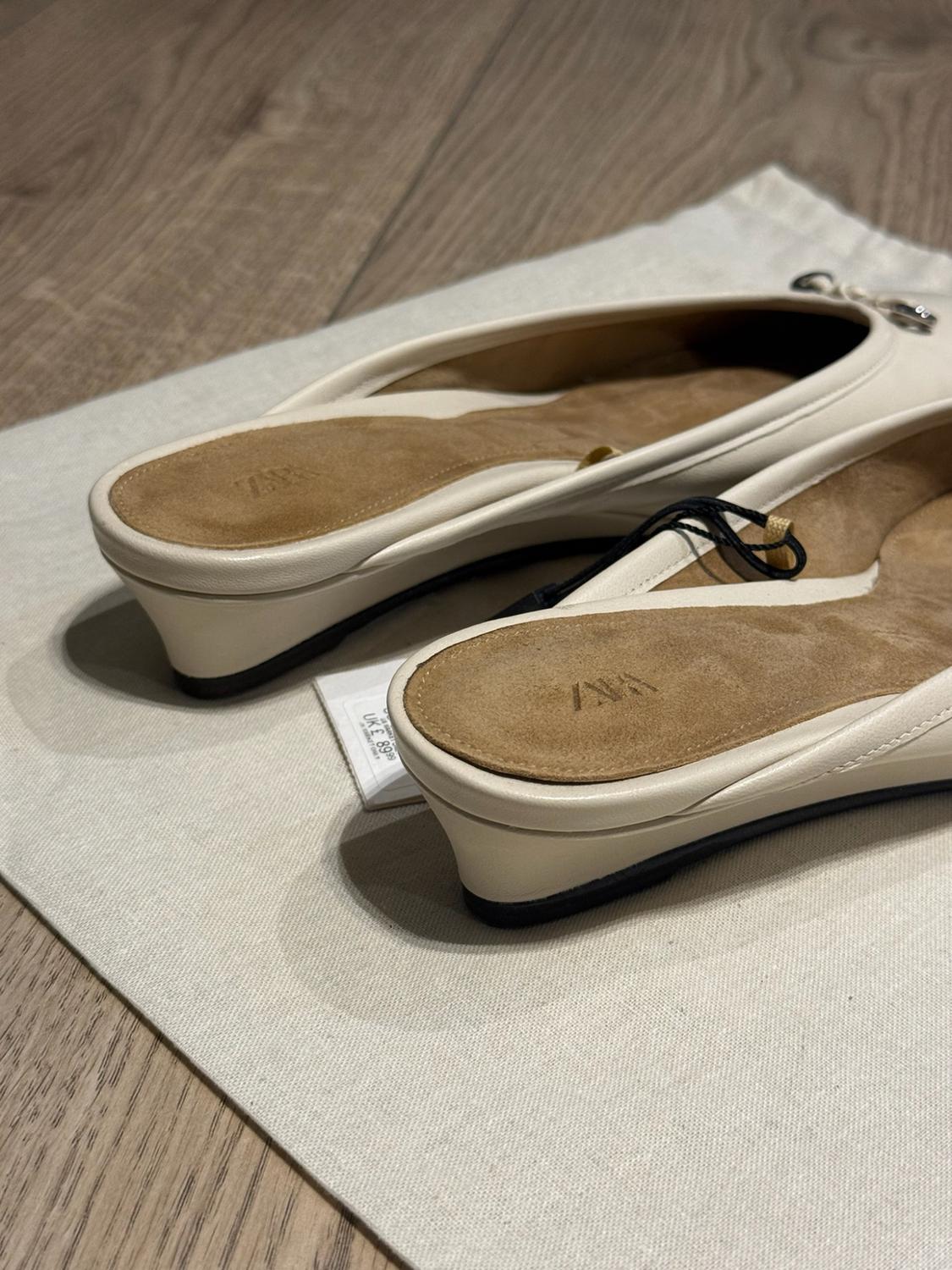 White slingback fabric shoes on a wooden floor. Inner sole with "ZARA" text and visible tag showing "UK £ 89.99".