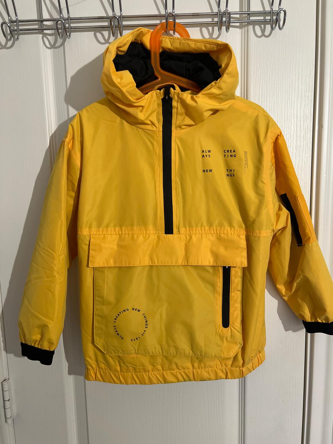 Yellow hooded jacket with a black zipper, hanging on a hanger. Visible text: "ALWAYS CREATING NEW THINGS".