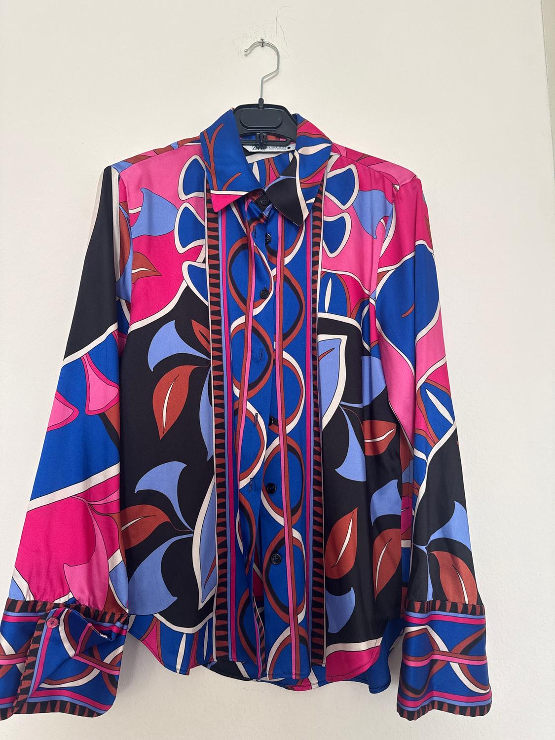Long-sleeved shirt with a geometric print in pink, blue, and black tones, hanging on a hanger against a white background.