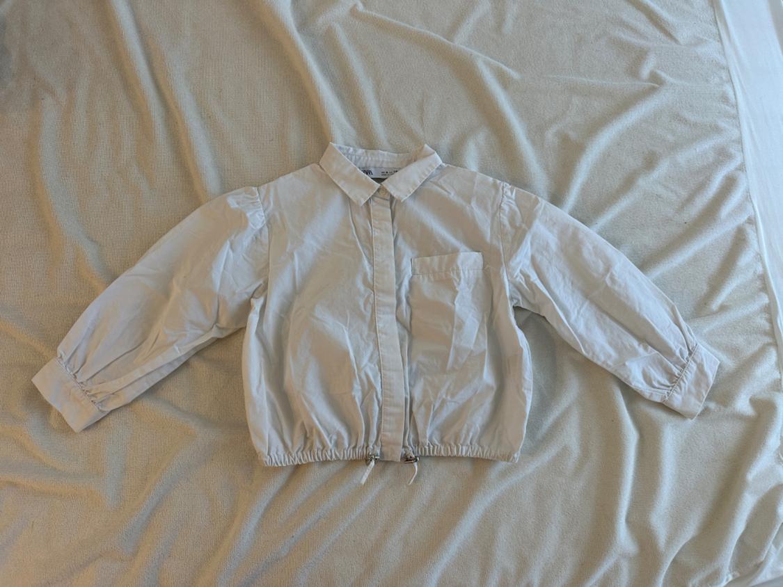 White, long-sleeved shirt with a breast pocket, laid on top of a crumpled beige cloth.