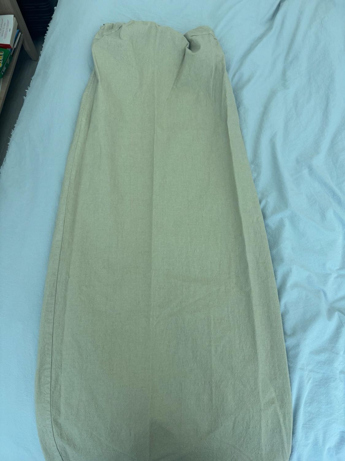Long strapless light green dress laid out on a bed with pale blue sheets.