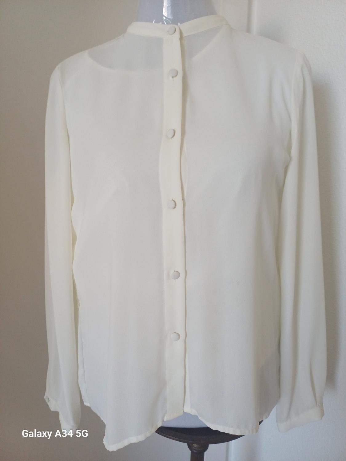 Front view of a white blouse with a central button fastening and a round neck.