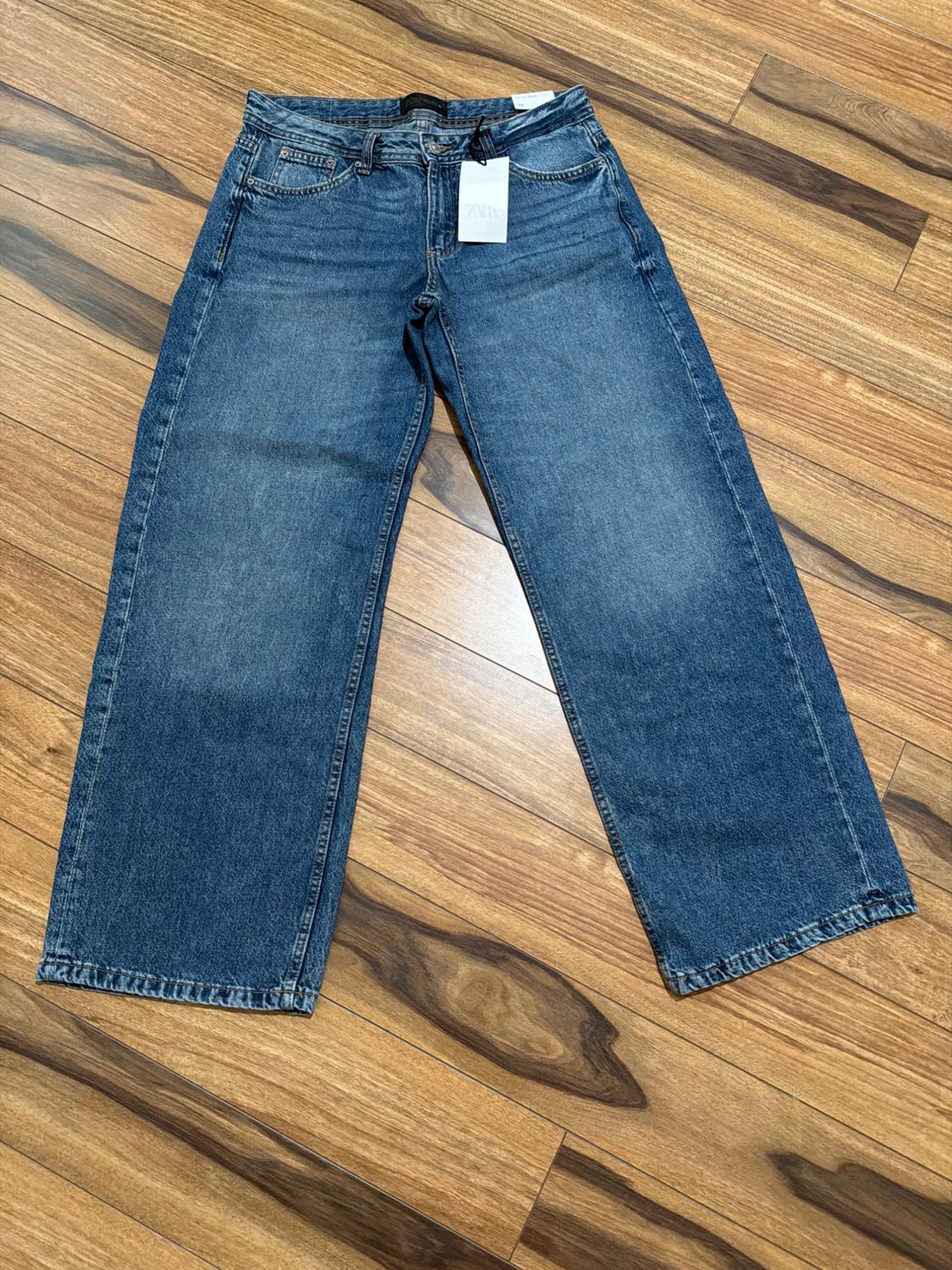 Mid-wash, wide-leg blue jeans, laid out on a wooden floor. White label with the text ZARA.