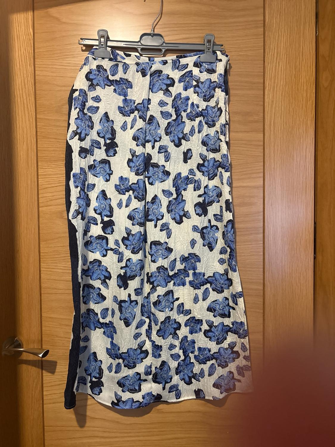 White maxi skirt with a blue floral print, hanging on a hanger on a wooden door.