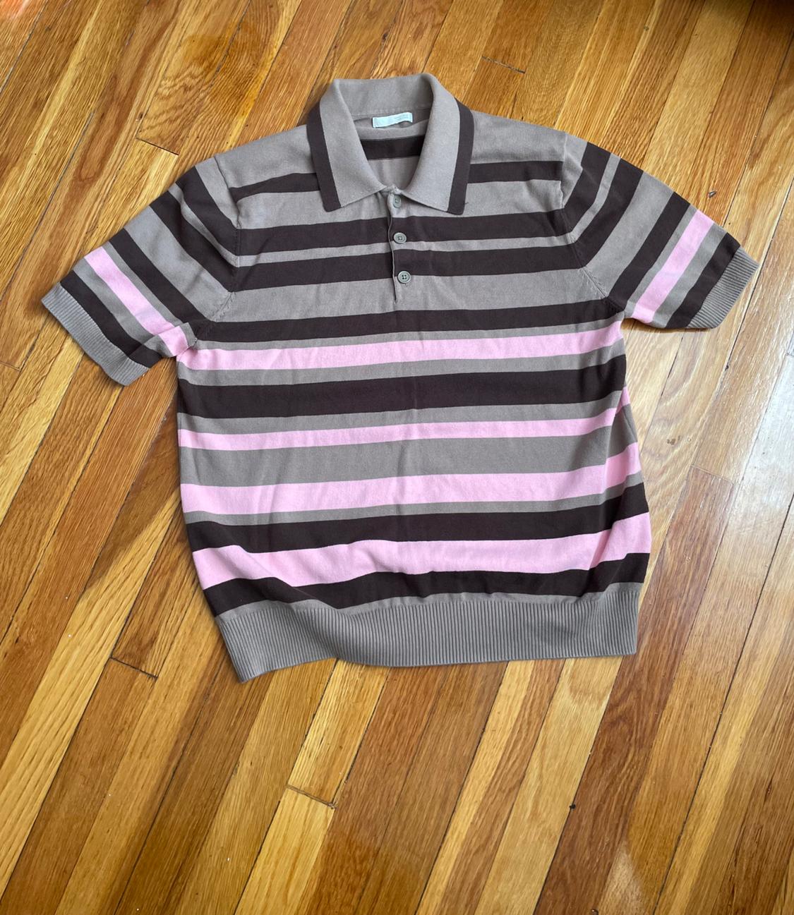 Short-sleeve polo shirt with horizontal stripes in shades of brown, beige, and pink, placed on a wooden floor.