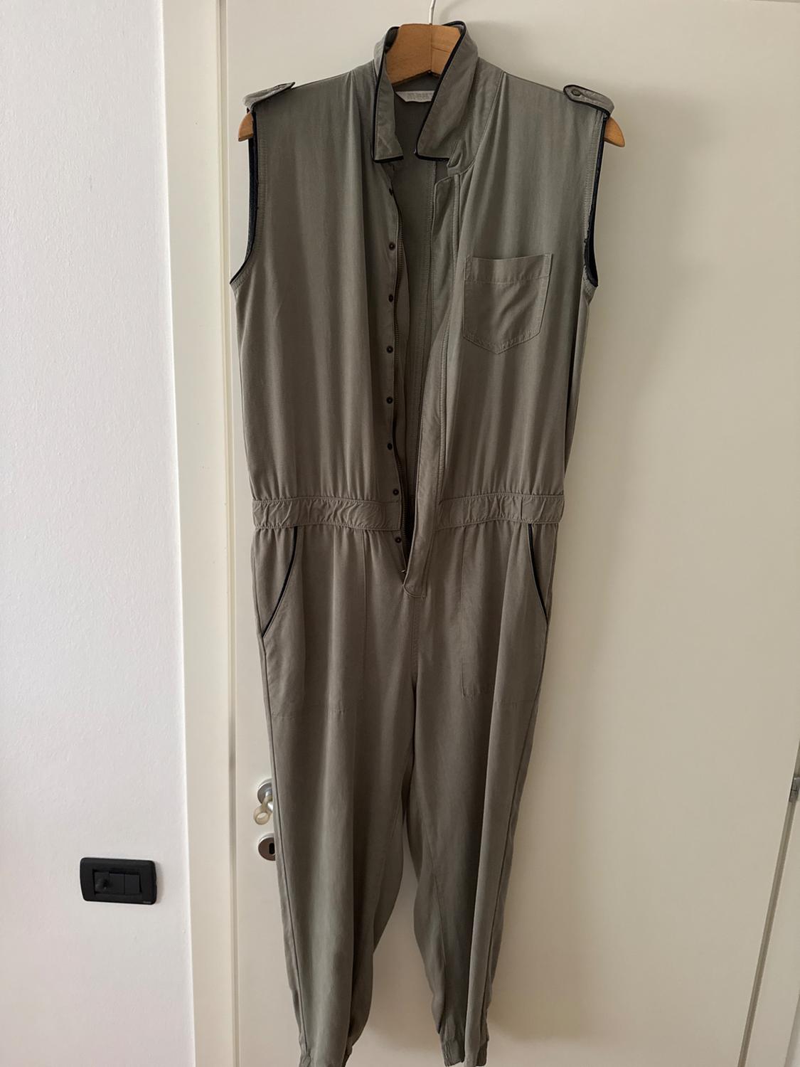Khaki sleeveless jumpsuit hanging on a wooden hanger over a white door, with pockets and front buttons.