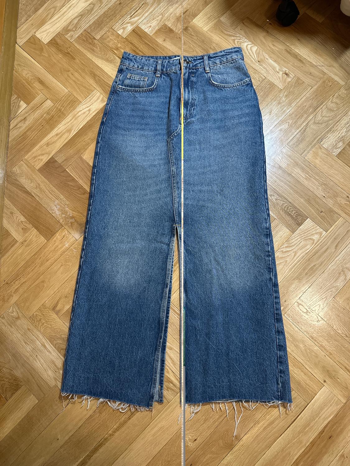 Wide-leg frayed hem jeans, placed on a light wooden floor.