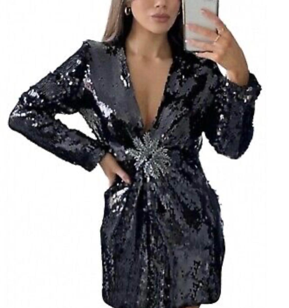 Woman in black sequin dress and sparkling brooch, taking a selfie in a mirror. White background.