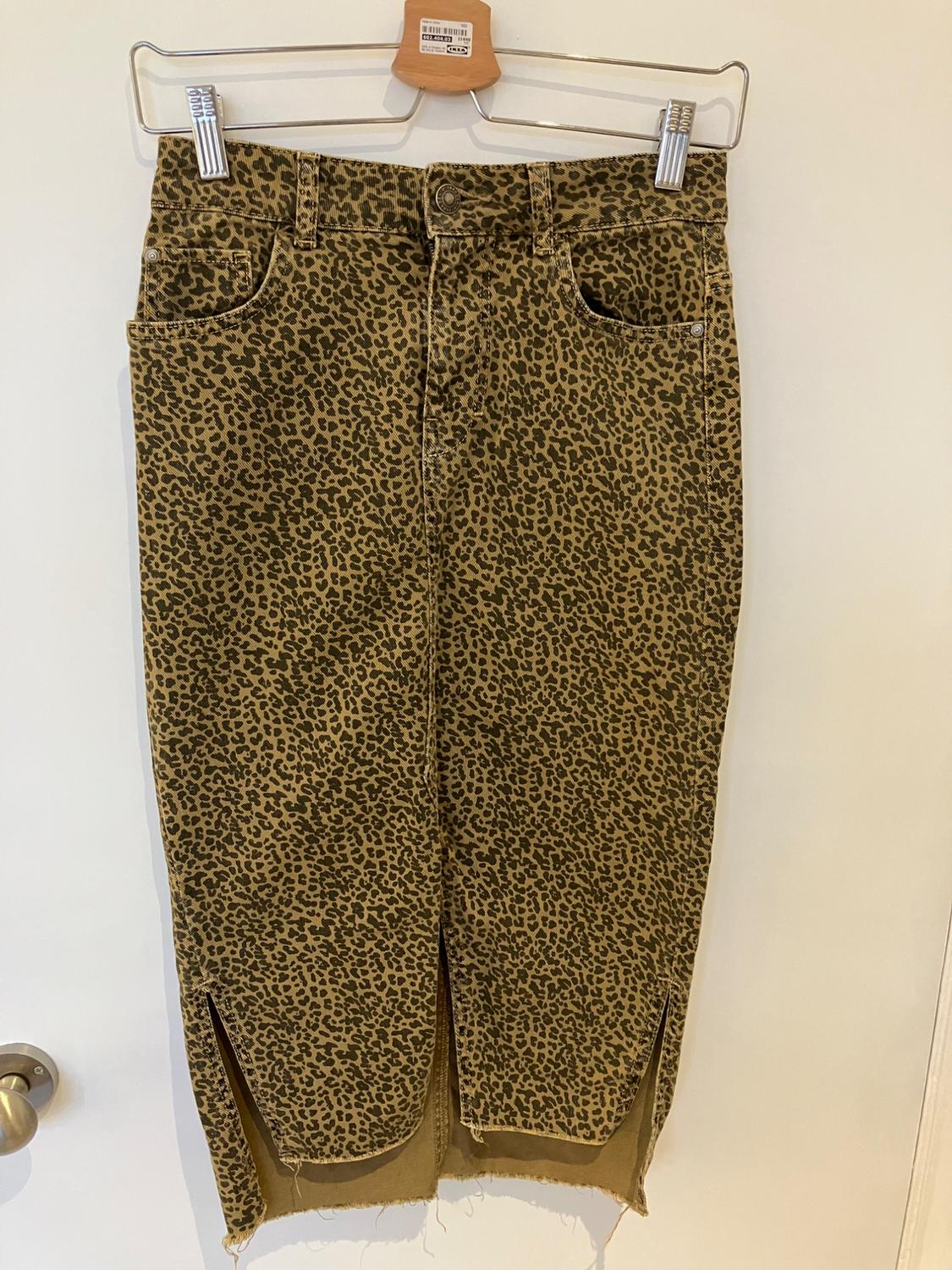 Leopard print denim midi skirt with a frayed hem and side slits, hanging on a wooden hanger.