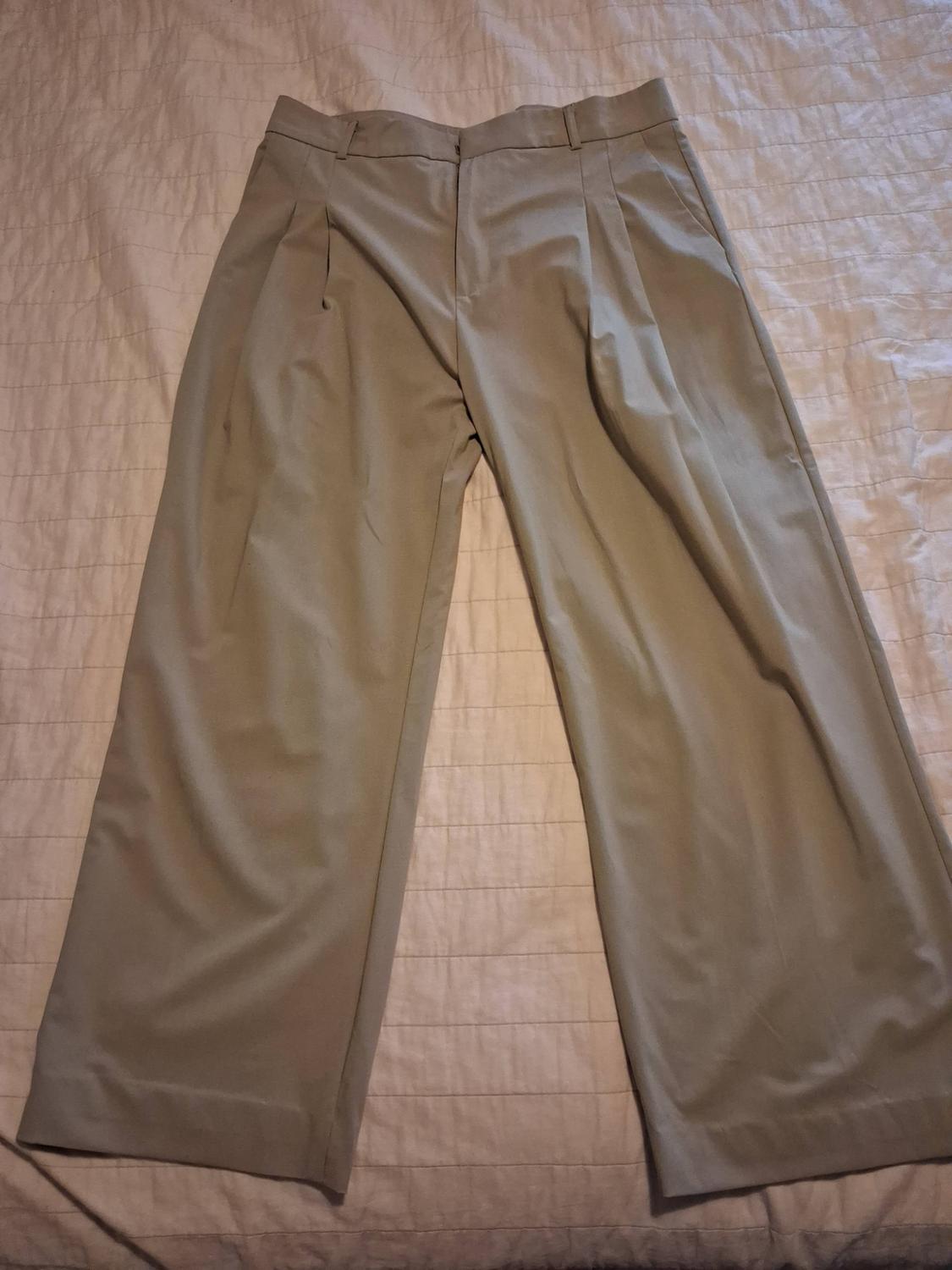 Beige wide-leg trousers with front pleats, laid out on a textured light fabric surface. Casual style.